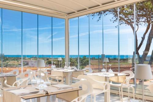 a restaurant with tables and chairs and large windows at Perla Saracena Hotel & Restaurant in Salve