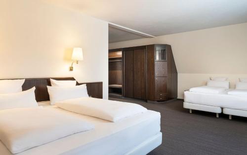 a white bedroom with two beds and a cabinet at elaya hotel noerdlingen, Trademark by Wyndham in Nördlingen