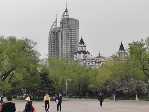 a group of people walking in a park with tall buildings at Central Street River View Apartment in Harbin