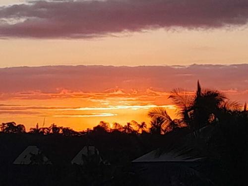 a sunset over a field with trees in the foreground at Samayra's Apartment in Nadi