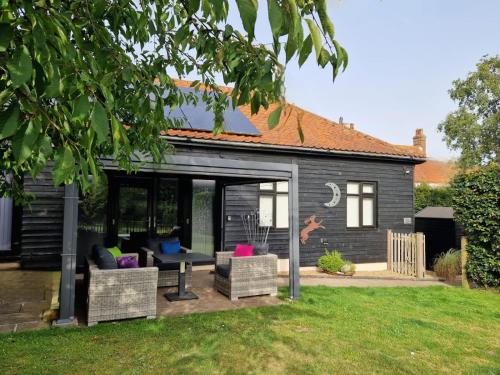 a black house with a patio with chairs at Swift Host - Owl Barn - Sleeps 2 - EV Charger - Pet Friendly in Loddon