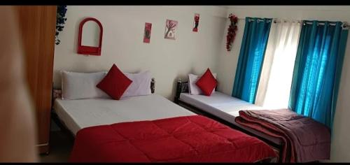 two beds in a bedroom with blue curtains and red pillows at Sreemoyee Homestay in Hatikhuli