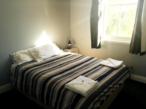 a bedroom with a bed with a striped blanket and a window at Kearsley Hotel in Cessnock