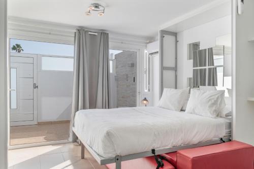 ein weißes Schlafzimmer mit einem großen Bett und einem roten Stuhl in der Unterkunft Estudio Kikere Puerto del Carmen in Puerto del Carmen