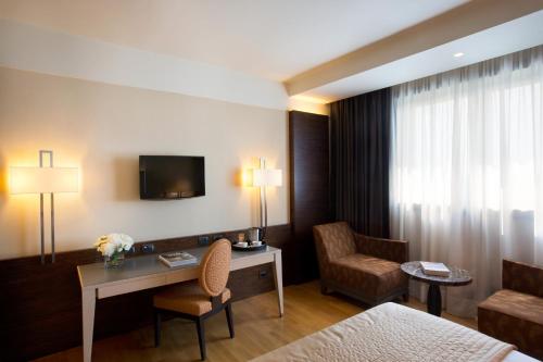 a hotel room with a bed and a desk and a tv at Starhotels Grand Milan in Saronno