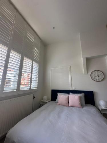 a bedroom with a bed with pink pillows and a clock at Comfortable City Break Studio in The Hague