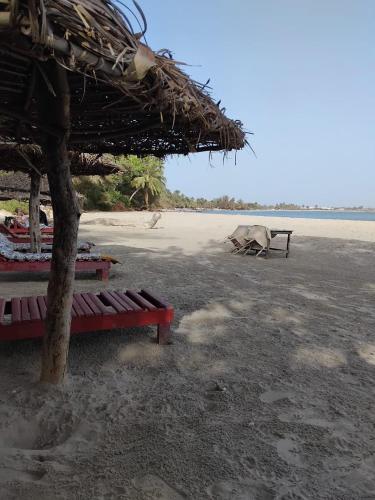 a beach with two red benches and a straw umbrella at Evergreen Eco Lodge Retreat in Tujering