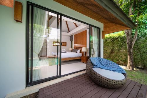 a bedroom with a bed and a wicker chair on a deck at BangTao Anchan 豪华两卧 私人泳池 现代度假巴厘风 in Layan Beach