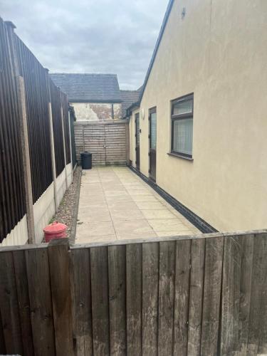 a wooden fence next to a building and a sidewalk at 2 bedroom bungalow, 15 minutes to Alton Towers, dog friendly in Wetleyrocks