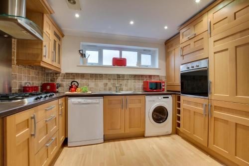 cocina con armarios de madera, lavadora y secadora en Beach Court, en Broadstairs