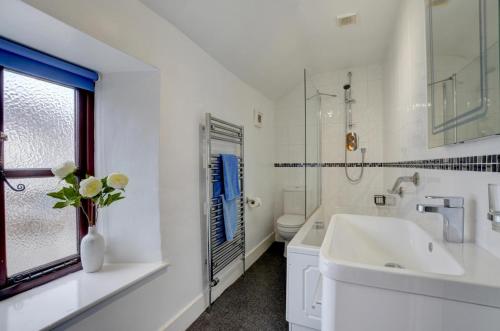 a white bathroom with a sink and a vase of flowers at Cross Farm Cottage in Braunton