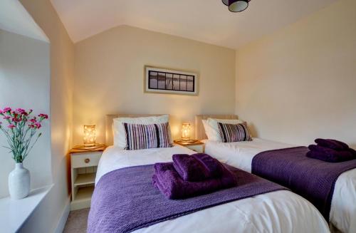 two beds in a room with purple blankets at Cross Farm Cottage in Braunton
