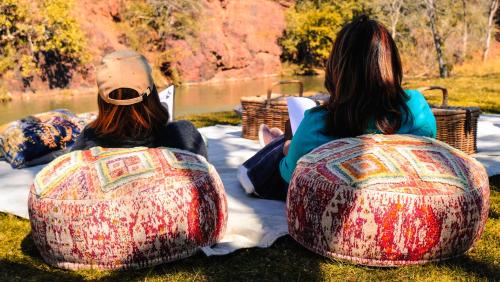 two women sitting on the grass next to a body of water at Mologa River Lodge in Rust de Winter