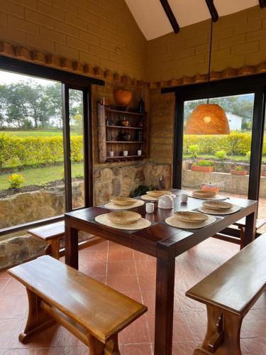 a dining room with a table and benches and windows at Hotel, Glampings y Cabaña Magic Bungalow in Villa de Leyva