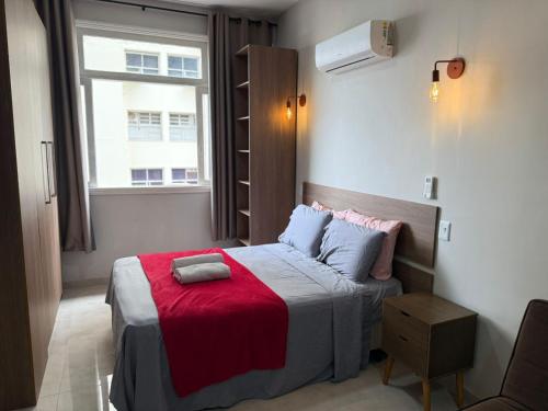 a bedroom with a bed with a red blanket and a window at Flat Centro Rio Av Presidente Vargas x Uruguaiana - Vista panorâmica do Cristo & Metrô in Rio de Janeiro
