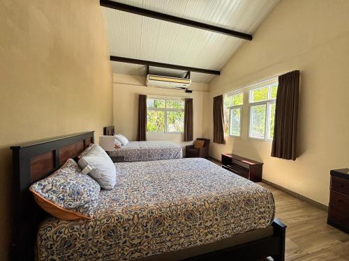 a bedroom with two beds and two windows at La Villa Suites el Quetzal in Lanquín