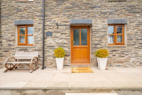 a stone building with a wooden door and two plants at Hafod y Llwynog in Cross Inn