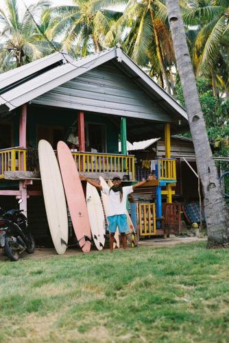 Pulau SarangにあるSurf House Hostelのサーフボードを持って家の前に立っている男性