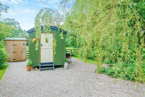 a green shed in a garden with a tree at The Harmony Hut in Skirwith