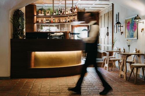 a woman walks past a bar in a restaurant at Strasserwirt - Ansitz zu Tirol in Strassen