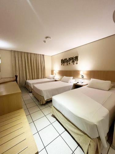 a hotel room with two beds and a room with two tables at Hotel Diogo in Fortaleza