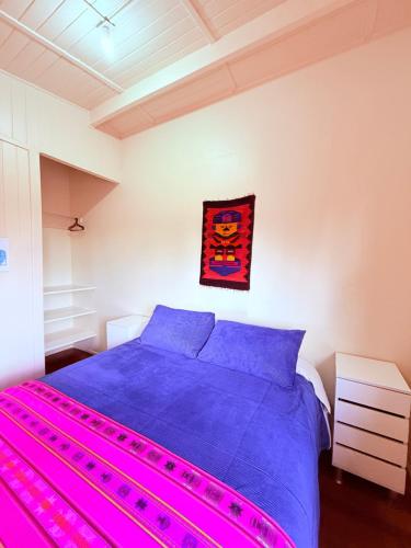a bedroom with a bed with purple sheets and a painting on the wall at MAKTVB - EcoLodge San Pedro de Atacama in San Pedro de Atacama
