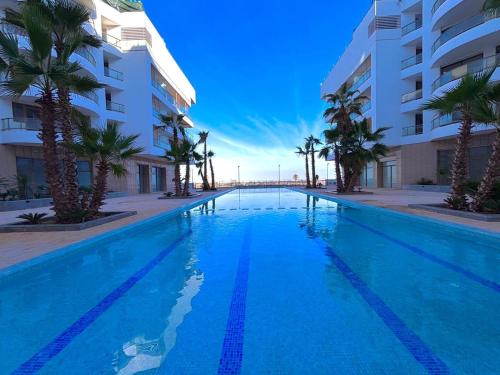 a swimming pool with palm trees in front of a building at La perla del Atlántico in Casablanca