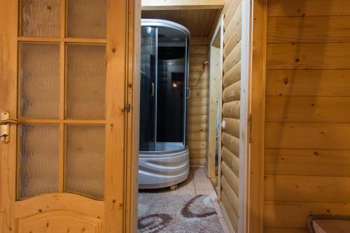 a walk in shower in a wooden room with a glass door at Хата Різьбяра in Beloberëzka