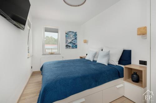 a white bedroom with a blue bed and a window at Apartament BEATA 102 Dziwnówek 200m od plaży EPapartamenty in Dziwnówek
