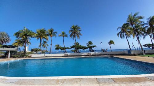 a swimming pool with palm trees and the ocean at Ocean View. Acogedor Apartamento frente al mar in Porlamar