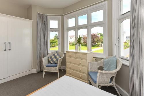 a bedroom with two chairs and a dresser and windows at 1 Coed y Llyn in Abersoch