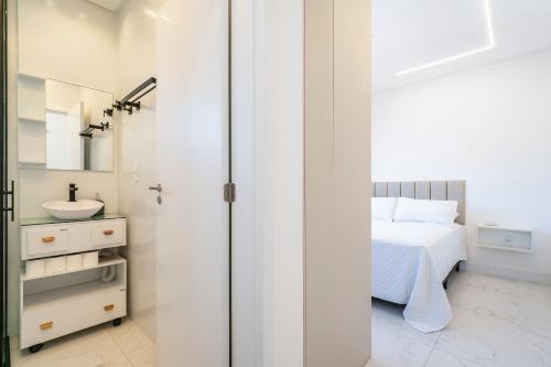 a white bedroom with a bed and a sink at Condomínio Green Ville Residence | Bombinhas | SC in Canto Grande