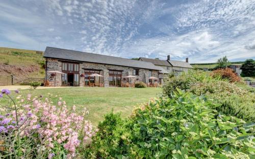 a large stone house with a yard with flowers at Threshing Barn in Bampton