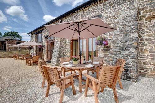 a wooden table with chairs and an umbrella at Threshing Barn in Bampton
