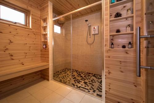 a shower with a glass door in a wooden bathroom at Ysgubor Bach in Aberdaron