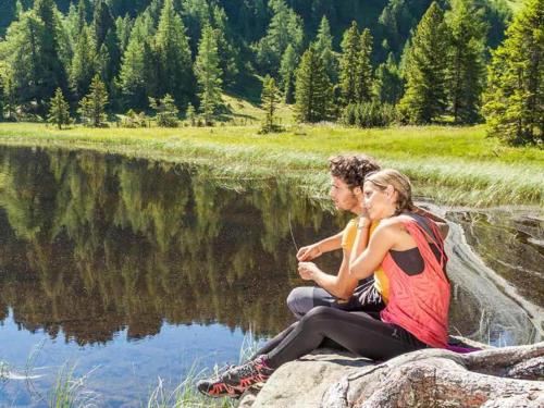 two people sitting on a rock near a lake at Grebenzen Lodge Hirsch in Sankt Lambrecht