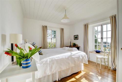 a white bedroom with a bed and a table with a vase of flowers at The White Cottage in Saint Winnow