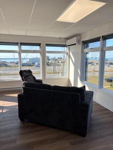 a black couch sitting in a room with windows at Auberge de la traverse in Matane