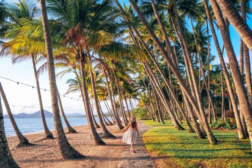 a woman walking down a path through palm trees on the beach at Belle Escapes Relax Rose in Palm Cove