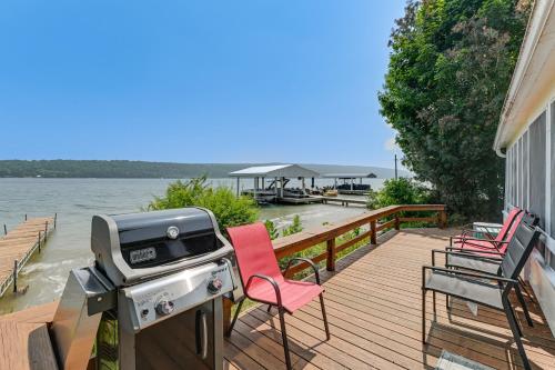 a deck with a grill and chairs on the water at Dock and Rowboat Beechnut Bungalow on Keuka Lake in Branchport