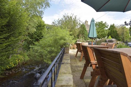 a patio with tables and an umbrella and a stream at Littlebeck in Kettlewell