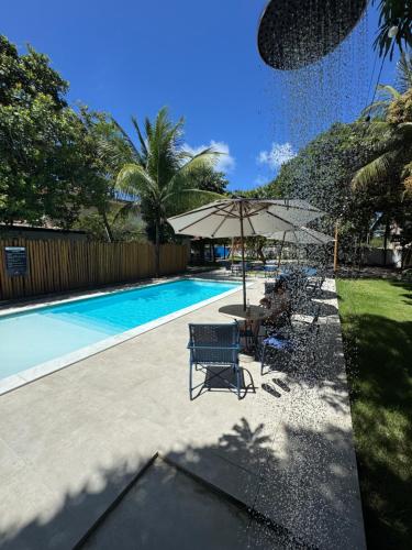 a swimming pool with a table and an umbrella at Pousada Porto Verano in Porto De Galinhas