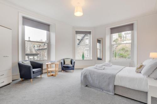 ein weißes Schlafzimmer mit einem Bett, Stühlen und Fenstern in der Unterkunft The Ambleside Loft in Ambleside