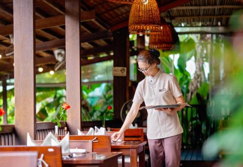 a woman standing in a restaurant holding a menu at Hoi An Eco Lodge & Spa in Hoi An