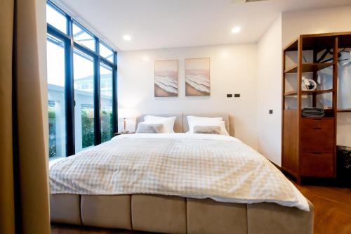 a bedroom with a large bed and large windows at Vita Villa - Modern 2BR At Heart of Phetchaburi in Phetchaburi