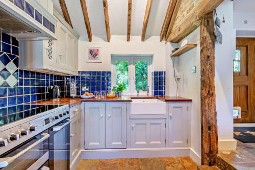 a kitchen with blue tiled walls and wooden beams at The Granary - Ticehurst in Ticehurst