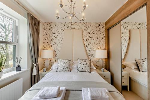 een slaapkamer met een bed met 2 ramen en een kroonluchter bij Charter Gardens Cottage in Kirkby Stephen