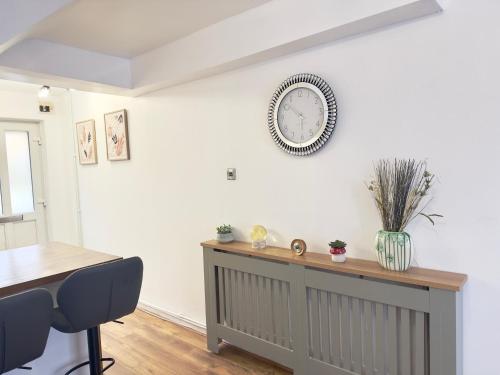 a dining room with a table and a clock on the wall at The Cozy Hideaway - 2 Bedroom apartment with garden in Orpington with free Parking in Foots Cray