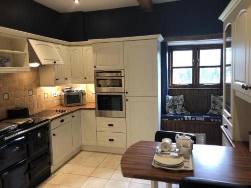 a kitchen with white cabinets and a wooden table at Woods Close at Sanctuary Farm in Kilkhampton