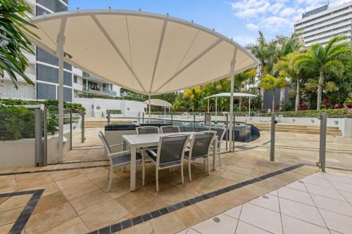 a patio with a table and chairs under a large umbrella at Beachside Penthouse w Private Rooftop & Oceanviews in Caloundra